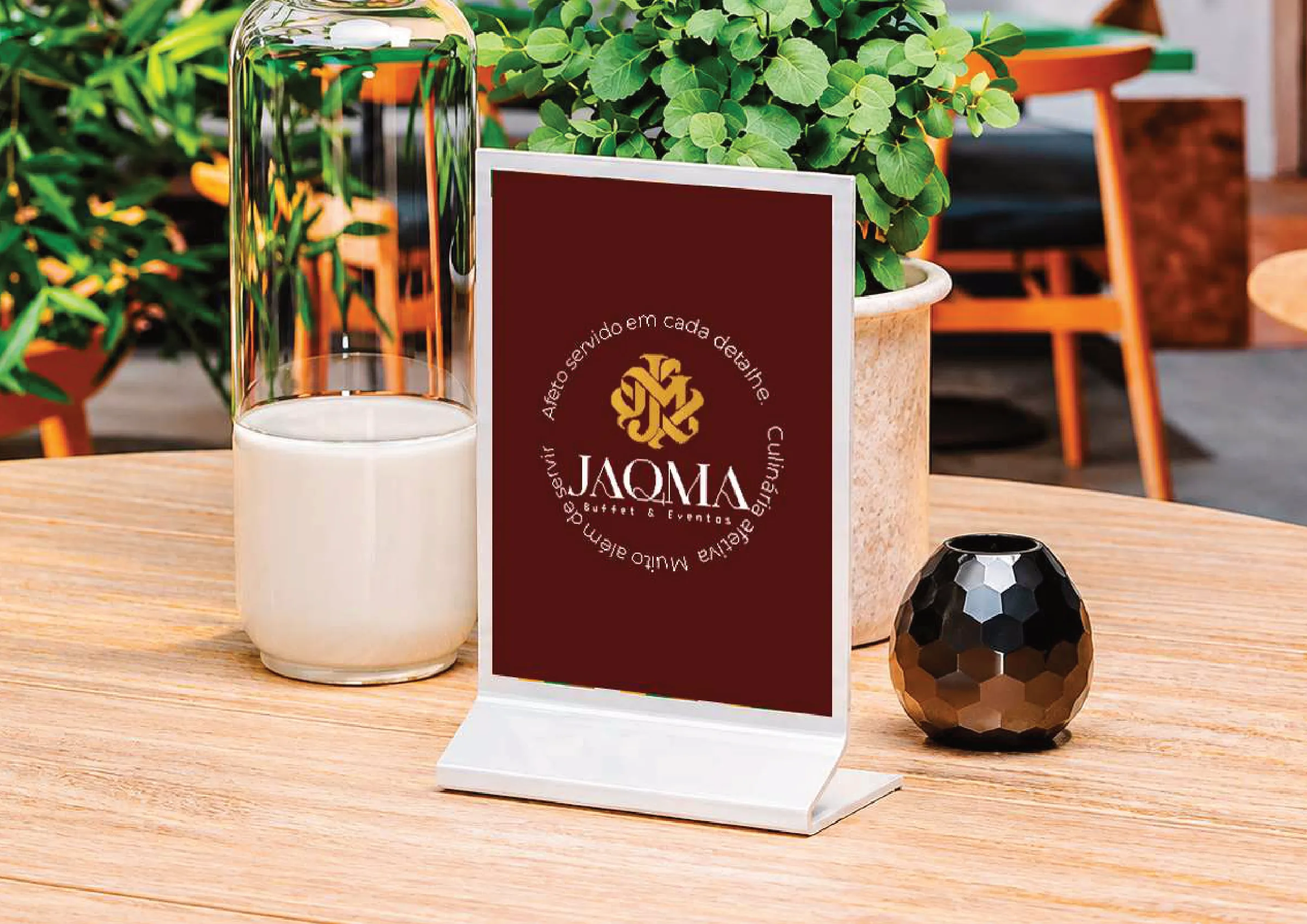 Display de mesa em bordô com o selo da JAQMA e a frase "Afeto servido em cada detalhe".