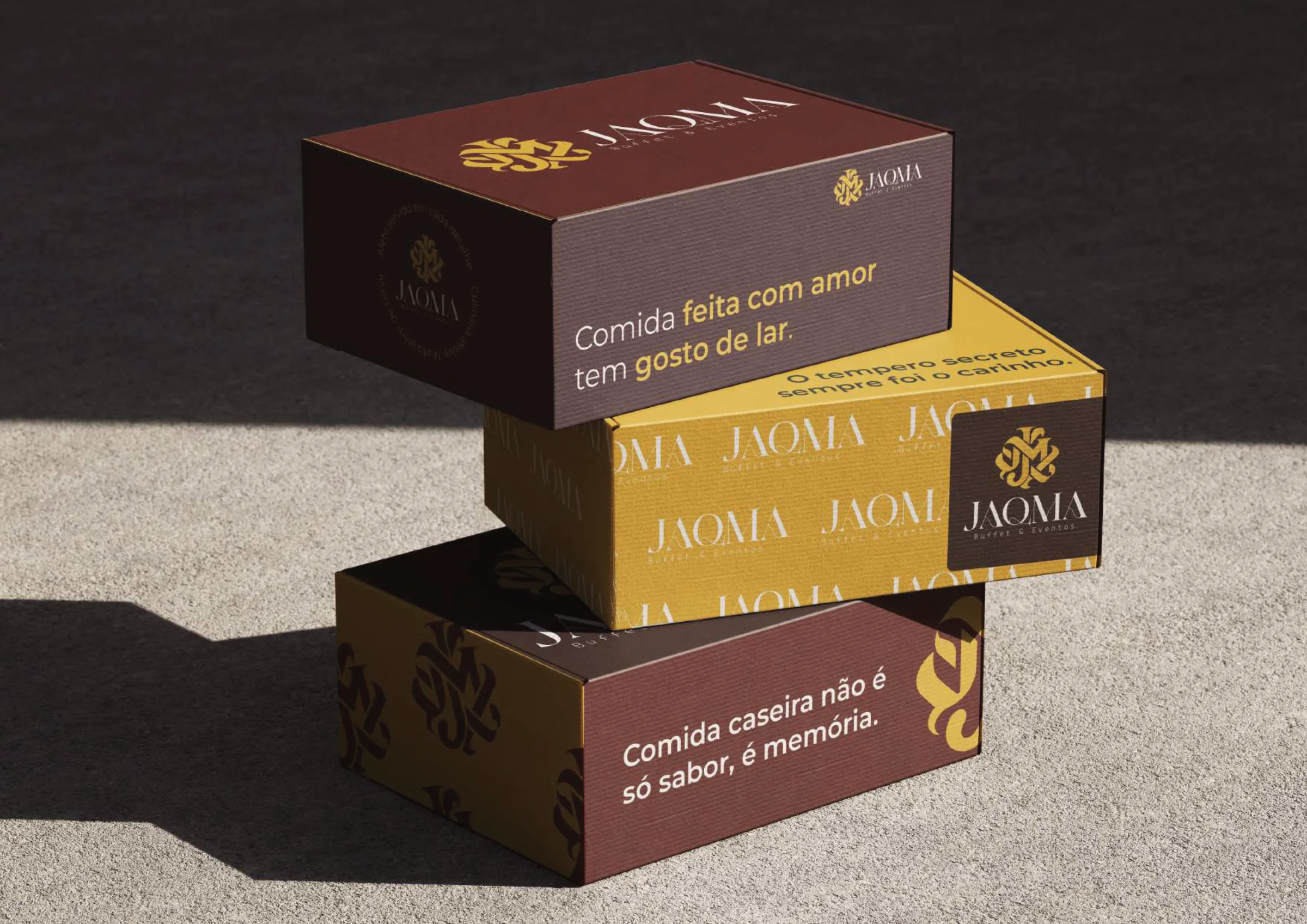 Caixas de embalagem da JAQMA em bordô, marrom e dourado com frases da marca.